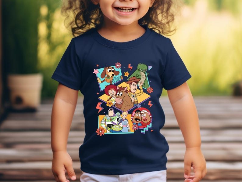 May include: Navy blue t-shirt featuring a colorful graphic of characters from the animated film "Toy Story." The design includes images of Woody, Buzz Lightyear, and other characters. The shirt is suitable for children.