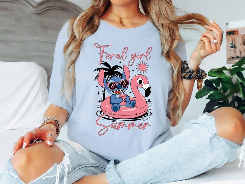 Pu&ograve; includere: T-shirt azzurra con un disegno di Stitch di Lilo & Stitch con occhiali da sole su un galleggiante a forma di fenicottero rosa. Il testo dice "Feral girl Summer" in rosa. Un design estivo e divertente.