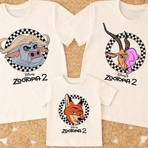 May include: Three white t-shirts with cartoon character graphics from Disney's Zootopia 2. Each shirt features a different character in a black and white checkered circle. The text "Zootopia 2" is printed below each graphic.