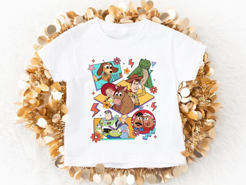 May include: White t-shirt featuring a colorful graphic of characters from the animated film Toy Story. The design includes Woody, Buzz Lightyear, and other characters in a retro style. The shirt is made of a soft material.