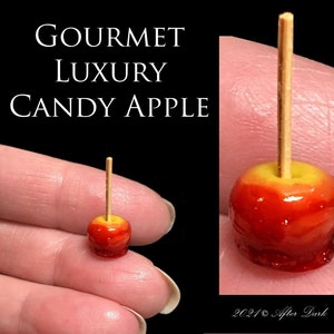 Puede incluir: Una manzana de caramelo en miniatura con un glaseado rojo y amarillo en un palo de madera. La manzana de caramelo es aproximadamente del tamaño de una moneda de 10 céntimos.