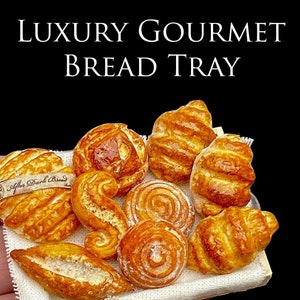 Puede incluir: Una bandeja de pan en miniatura con una variedad de productos horneados, incluyendo cruasanes y panecillos. La bandeja es de madera y está forrada con tela blanca. El texto "LUXURY GOURMET BREAD TRAY" es visible.