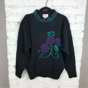 May include: Black sweater with a high mock neck and a floral design in purple, green, and white. The sweater has the text "J.Jill" on the inside of the neck.
