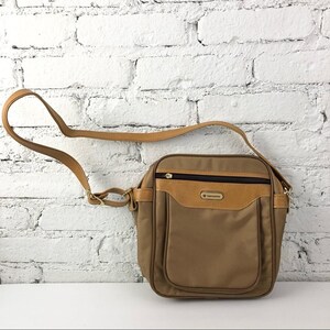 Pode incluir: Bolsa transversal Samsonite marrom com um detalhe em couro bege na frente e uma longa alça ajustável. A bolsa tem um zíper na parte superior e um pequeno logotipo na frente.