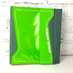 May include: A green Trapper Keeper binder with a white border and the text "Trapper Keeper" in white. The binder has a bright green front and a darker green spine and edges. The Mead logo is visible in the upper left corner.