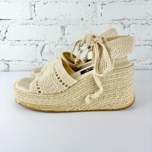 Op de afbeelding: Beige espadrille sleehak sandalen met een geweven jute platform en haakdetails. De sandalen hebben een peep-toe design en enkelbandjes. Het platform meet ongeveer 7.6 cm.