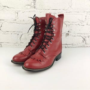 May include: A pair of red leather lace-up boots with fringe detailing. The boots have a pointed toe and a stacked heel.