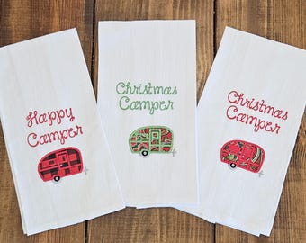 Puede incluir: Tres paños de cocina blancos con diseños de caravanas bordados. Una toalla dice "Happy Camper" con una caravana roja y negra. Las otras dos dicen "Christmas Camper" con diseños de caravanas rojas y verdes.