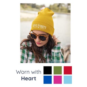 May include: Mustard yellow beanie with the text "LOVE & UNITY" in white. The beanie is worn with tortoise shell sunglasses and a green and white plaid shirt. The image also includes a colour palette.