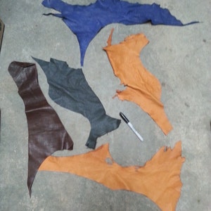 May include: Five pieces of leather in different colors and shapes. The leather is blue, brown, and orange. The leather pieces are arranged on a gray surface.