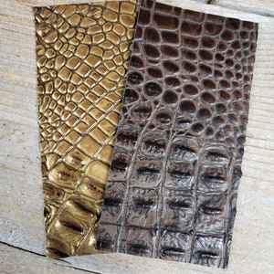 K&ouml;nnte beinhalten: Zwei St&uuml;cke Kunstkrokoleder in Gold und Braun. Das Leder hat ein strukturiertes, gepr&auml;gtes Muster.