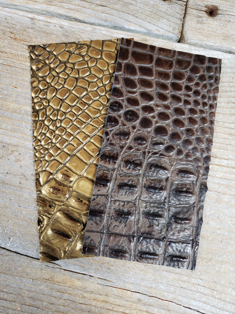 K&ouml;nnte beinhalten: Zwei St&uuml;cke Kunstkrokoleder in Gold und Braun. Das Leder hat ein strukturiertes, gepr&auml;gtes Muster.