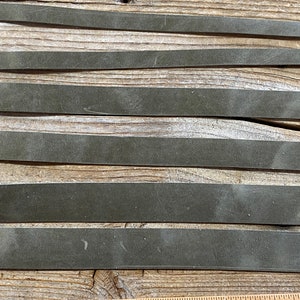 May include: Six strips of dark green leather laid out on a wooden surface.