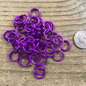 May include: A pile of purple metal jump rings, approximately the size of a US quarter.