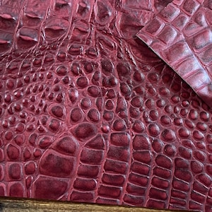 May include: Close-up of a burgundy faux crocodile leather fabric with a textured, embossed pattern.