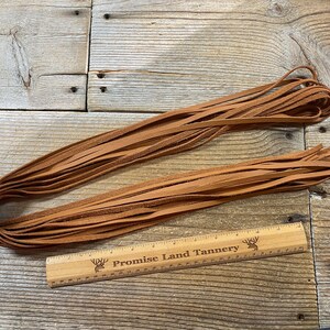 May include: A bundle of brown leather strips, approximately 12 inches long, laid out on a wooden surface. A ruler with the text "Promise Land Tannery" is placed next to the leather strips.