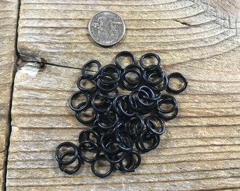 May include: A pile of black jump rings, approximately the size of a US quarter, on a wooden surface.