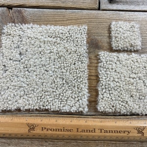 May include: Three white sheepskin rug samples of different sizes. The samples are laid out on a wooden surface with a ruler that reads "Promise Land Tannery".