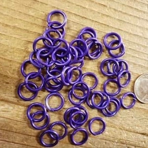 May include: A pile of purple metal jump rings. The rings are small and are about the size of a US quarter.