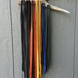 May include: A set of leather cords hanging from a wooden antler rack. The cords are in various colors, including black, brown, orange, yellow, and blue.