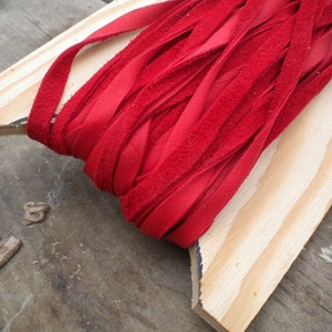 May include: A spool of red suede leather cord, wound around a wooden dowel. The cord is approximately 1.2 cm wide and is ideal for crafting projects.