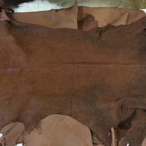 May include: A large piece of brown leather with a rough texture. The leather has been cut into an irregular shape and has a few small holes in it.