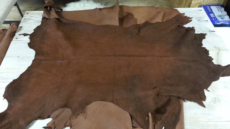 May include: A large piece of brown leather with a rough texture. The leather has been cut into an irregular shape and has a few small holes in it.