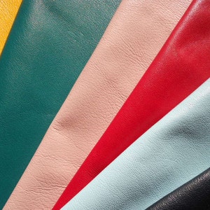 May include: A close-up of six different colored leather swatches. The swatches are arranged in a diagonal pattern, with the yellow swatch at the top left and the black swatch at the bottom right. The colors of the swatches are yellow, teal, light pink, red, light blue, and black.