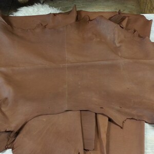 May include: A large piece of brown leather with a rough texture. The leather is folded in half and has a few tears along the edges.