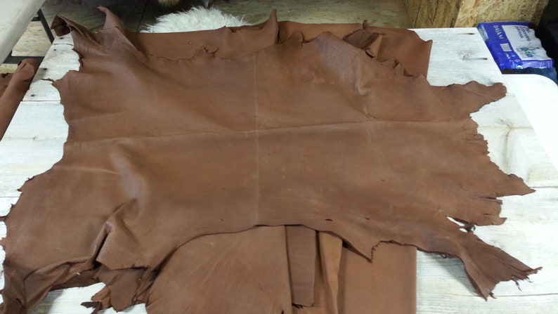 May include: A large piece of brown leather with a rough texture. The leather is folded in half and has a few tears along the edges.