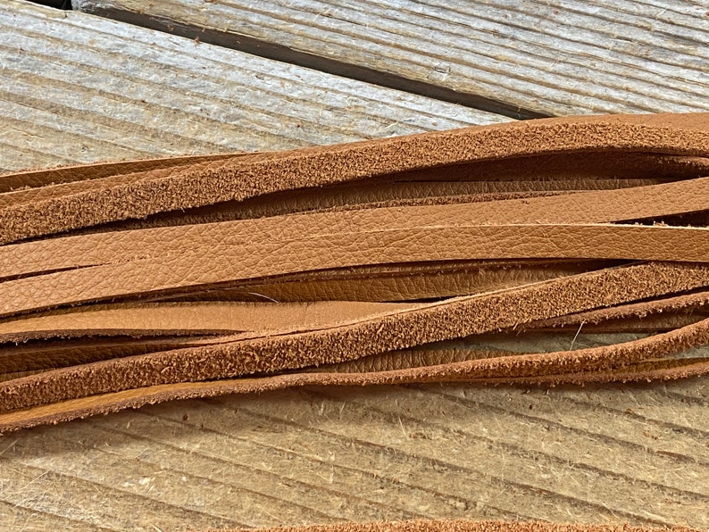 May include: A close-up of a bundle of brown leather strips. The leather is smooth on one side and has a slightly rough texture on the other side.