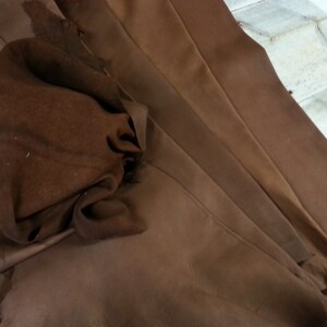 May include: A brown leather hide with a folded section. The leather has a rough, textured surface.