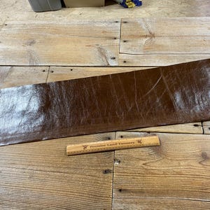 May include: A brown leather sheet with a textured surface. The sheet is lying on a wooden surface with a wooden ruler that says "Premier Land Tannery".