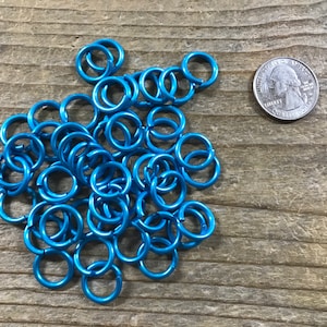 May include: A pile of small, bright blue metal jump rings. The rings are about the size of a US quarter.