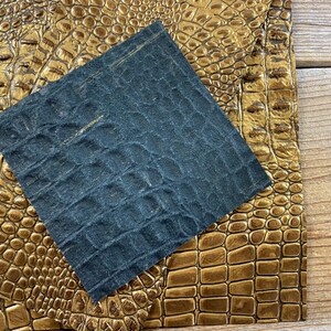 May include: A close-up of two pieces of faux leather. One piece is a dark blue with a textured alligator pattern. The other piece is a gold color with a textured alligator pattern.