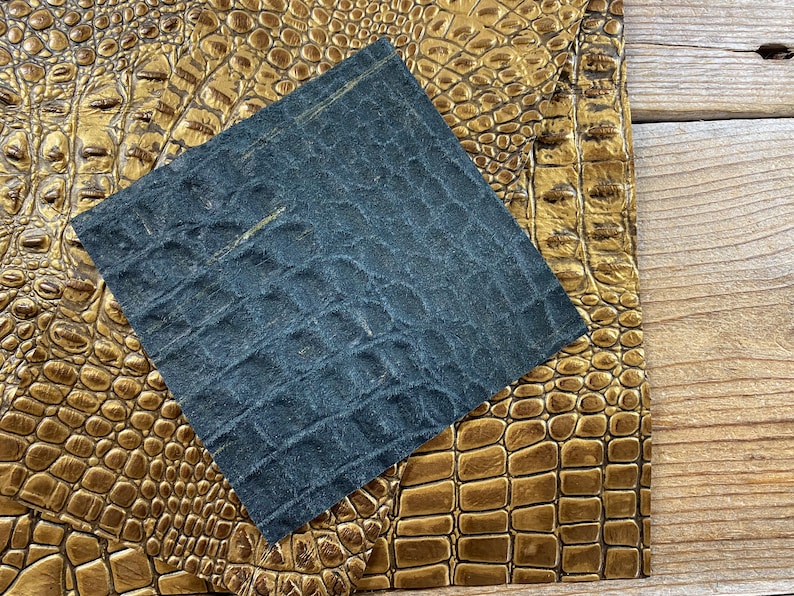 May include: A close-up of two pieces of faux leather. One piece is a dark blue with a textured alligator pattern. The other piece is a gold color with a textured alligator pattern.