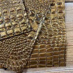 May include: Three pieces of gold faux crocodile embossed leather. The leather has a textured, pebbled surface.