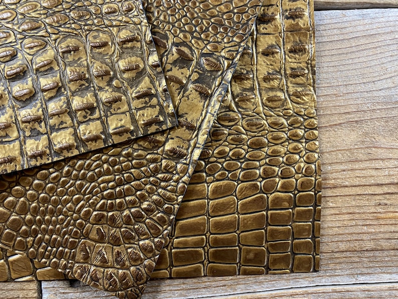 May include: Three pieces of gold faux crocodile embossed leather. The leather has a textured, pebbled surface.