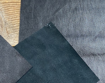 May include: Two pieces of black leather with a textured surface. The leather is laid out on a wooden surface.