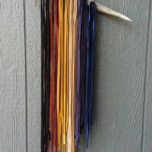 K&ouml;nnte beinhalten: Ein Satz Lederstreifen in verschiedenen Farben, darunter Schwarz, Braun, Gelb, Beige und Lila, die an einem Holzgeweih h&auml;ngen.