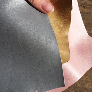 May include: Three pieces of leather in pink, gold, and gray. The leather is textured and has a slight sheen.