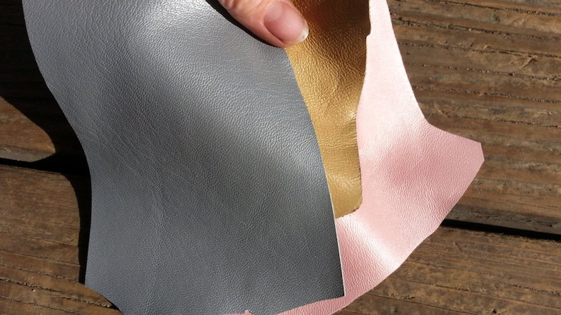 May include: Three pieces of leather in pink, gold, and gray. The leather is textured and has a slight sheen.
