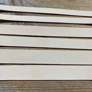 May include: Five strips of off-white leather laid out on a wooden surface.