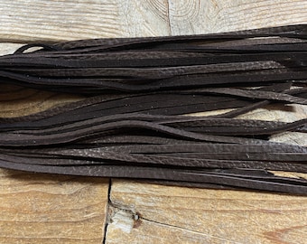 Puede incluir: Un manojo de flecos de cuero marrón oscuro, probablemente para manualidades o decoración.