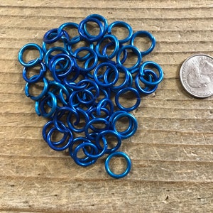 May include: A pile of blue metal jump rings, approximately the size of a US quarter.