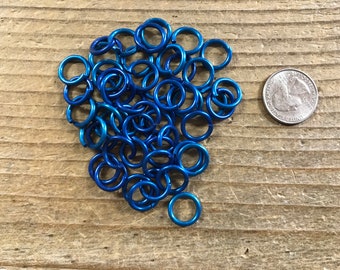 May include: A pile of blue metal jump rings, approximately the size of a US quarter.