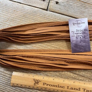 May include: A bundle of 10 cinnamon colored leather lacing strips, each measuring 1/4 inch wide by 72 inches long. The strips are stacked neatly on a wooden surface. The label reads "SKU: 221215-BBB Cinnamon Co Lacing 1/4" x 72" QTY: 10" and is from Promise Land Tannery.