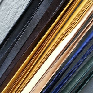 May include: Assortment of leather strips in various colors, including black, brown, yellow, beige, blue, and green. The strips are arranged in a diagonal pattern, showcasing their different textures and widths.