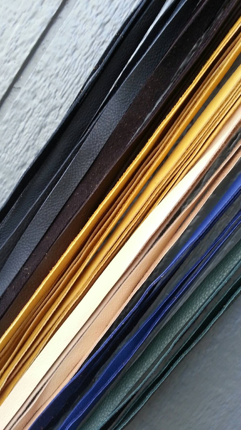 May include: Assortment of leather strips in various colors, including black, brown, yellow, beige, blue, and green. The strips are arranged in a diagonal pattern, showcasing their different textures and widths.