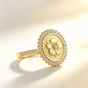 May include: A gold ring featuring a circular face with a raised five-petaled flower design in the center. The circular face is bordered by a halo of small, clear, round-cut stones, and the band is also set with a row of matching clear stones.